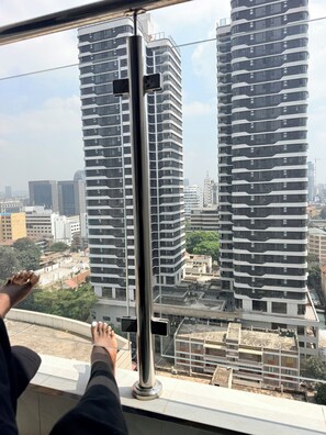 A view from a window with a metal pole, overlooking modern high-rise buildings and a construction site. - Spacious 2BR Westlands (Nairobi)