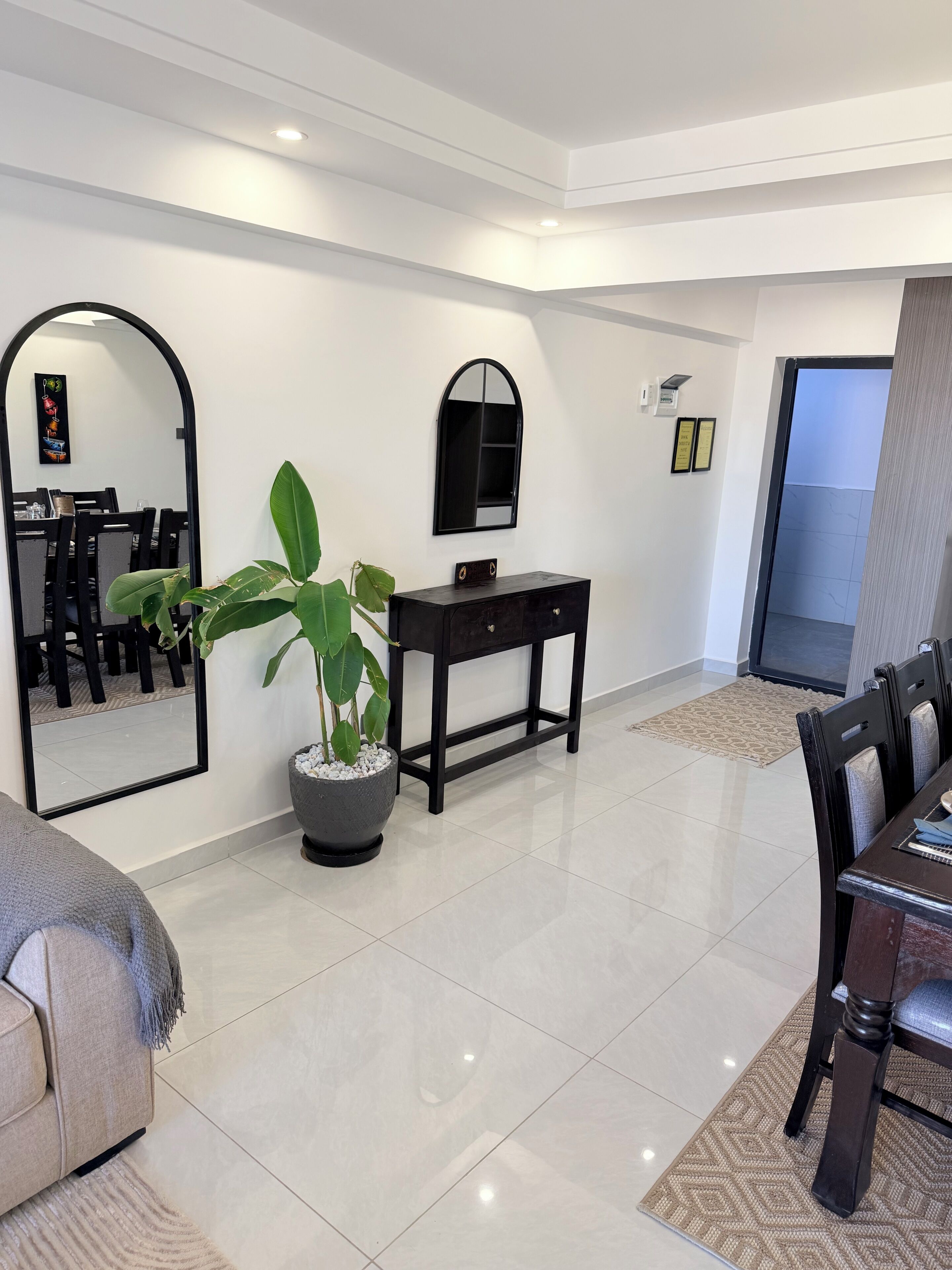A modern living room with a dining area, a large mirror, a potted plant, and a small table with a decorative item.