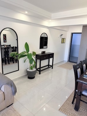 A modern living room with a dining area, a large mirror, a potted plant, and a small table with a decorative item. - Spacious 2BR Westlands (Nairobi)