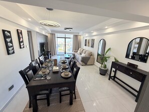 A modern dining room with a long table set for six, a sofa, a mirror, and a potted plant. - Spacious 2BR Westlands (Nairobi)