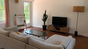 Un salon comprenant un canapé, un téléviseur, un cactus, une lampe et un tableau blanc sur lequel est écrit un message de bienvenue.