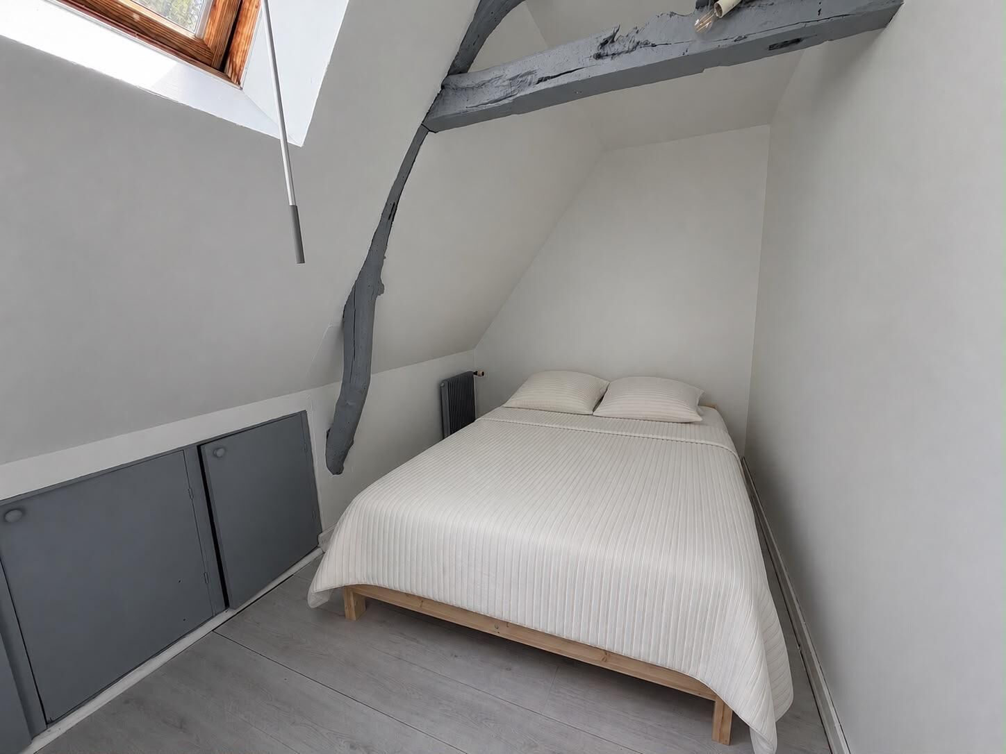 Quarto com teto inclinado, cama, radiador e janela.