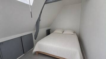 Quarto com teto inclinado, cama, radiador e janela.