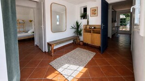 Une pièce comprenant un lit superposé, un miroir, un banc, une armoire et une porte donnant sur un espace extérieur.