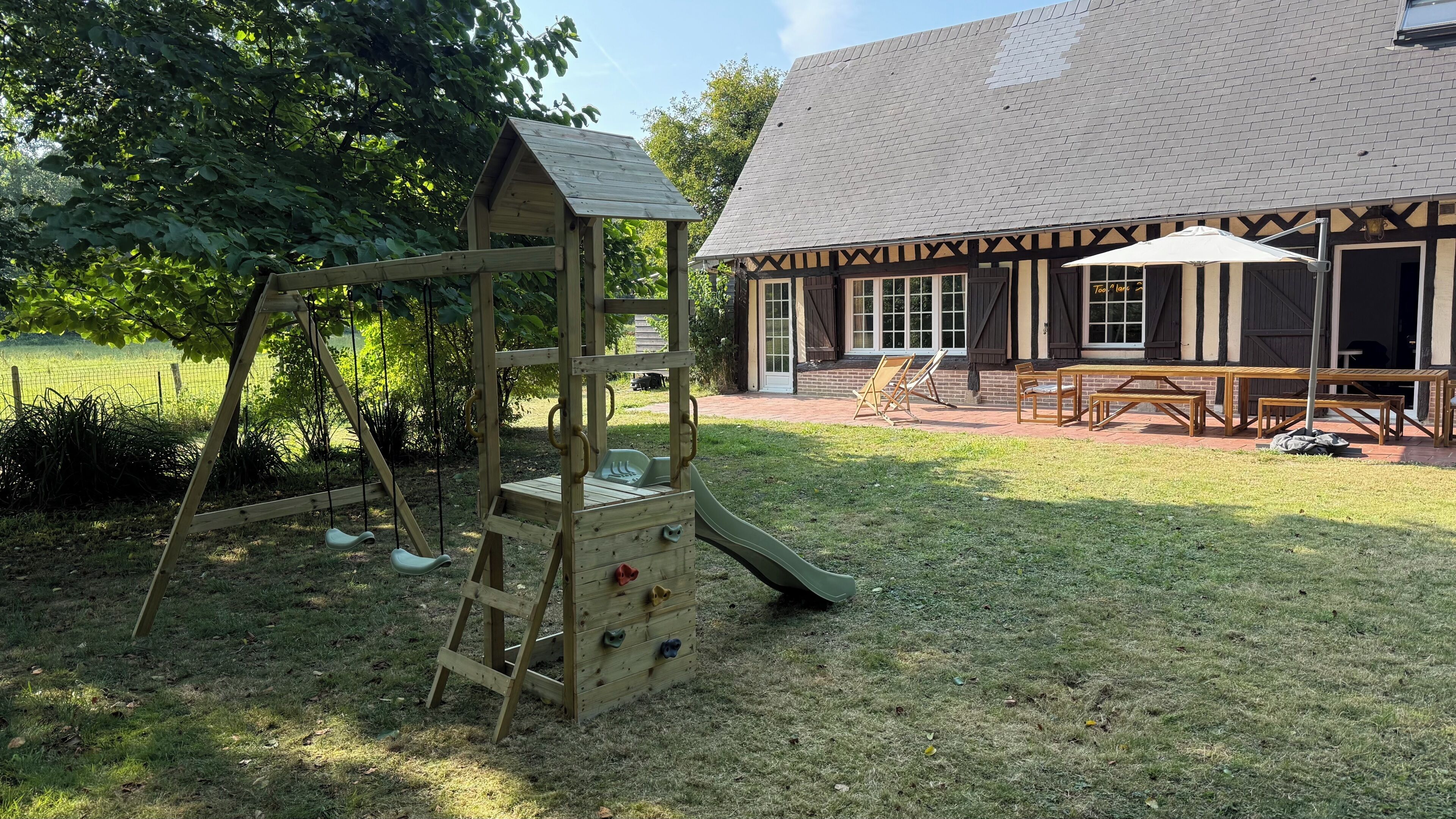 Una estructura de juego de madera y mesas de picnic en un área verde, con un edificio al fondo.
