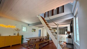 Une cuisine spacieuse avec une table en bois et des placards jaunes, un escalier et un panneau lumineux au néon.