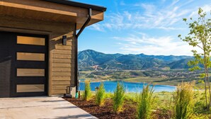 Ein modernes Haus mit Garage, Auffahrt und Blick auf einen See und Berge.