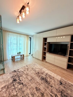 A modern living room with a large TV, wooden flooring, a patterned rug, and a glass partition. - Comfort and elegance in downtown Bucharest (București)
