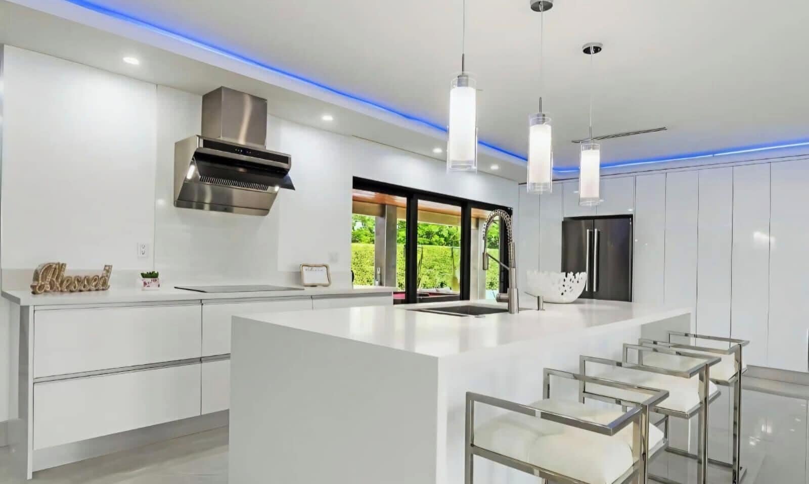 A modern kitchen with a central island, pendant lighting, and a view of greenery outside.
