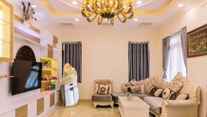 A living room with a flat-screen TV, a sofa, a coffee table, and a chandelier. - Hoanglee Villa (Mang Yang)