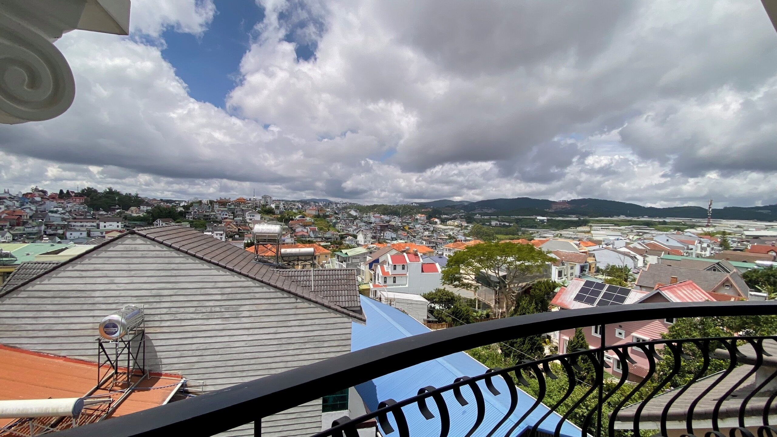 Ein Balkon mit Blick auf eine Stadt, darunter Geb äude und ein ferner Gebirgszug.