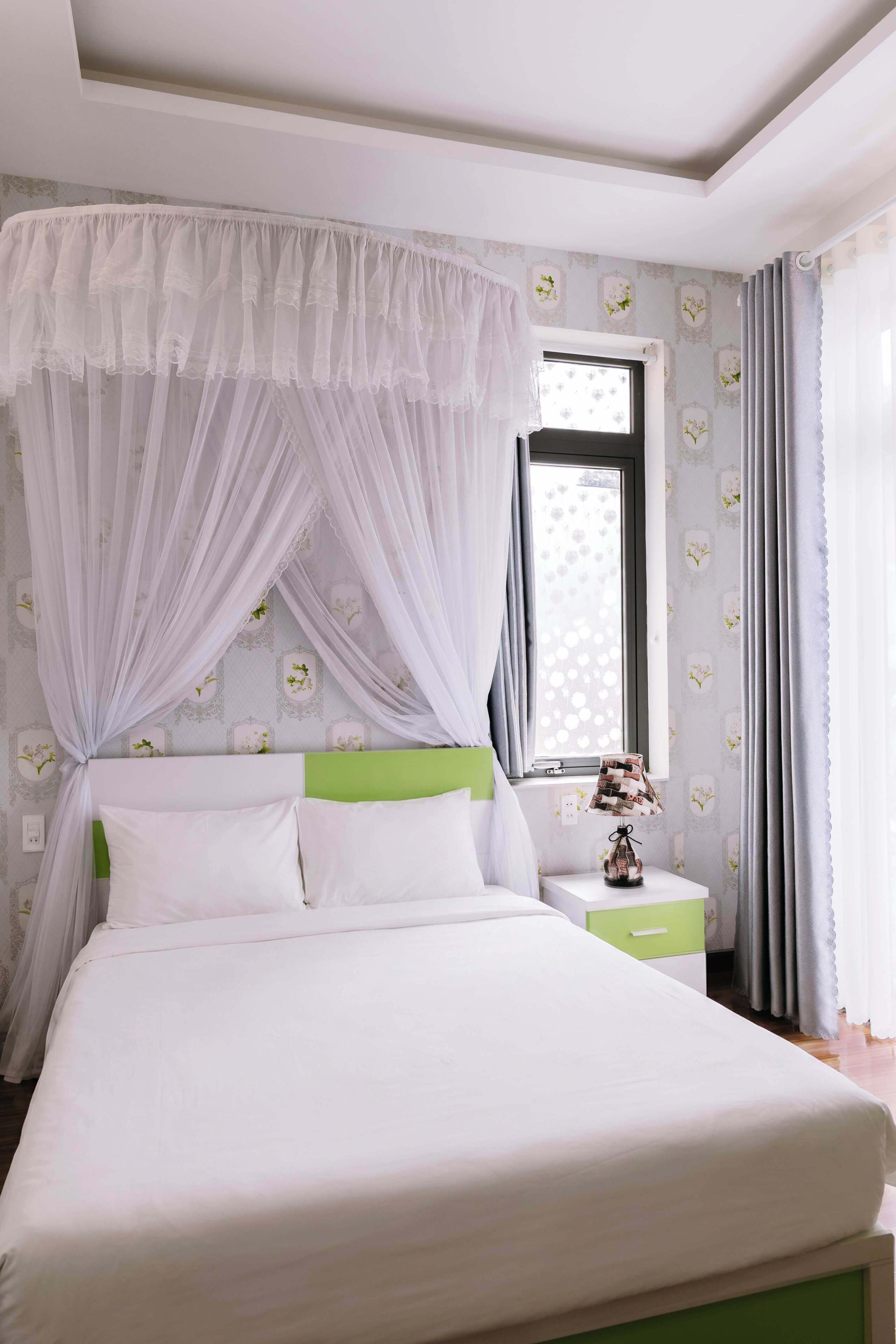 Un lit avec une tête de lit verte, une table de chevet avec une lampe et une fenêtre avec des rideaux.