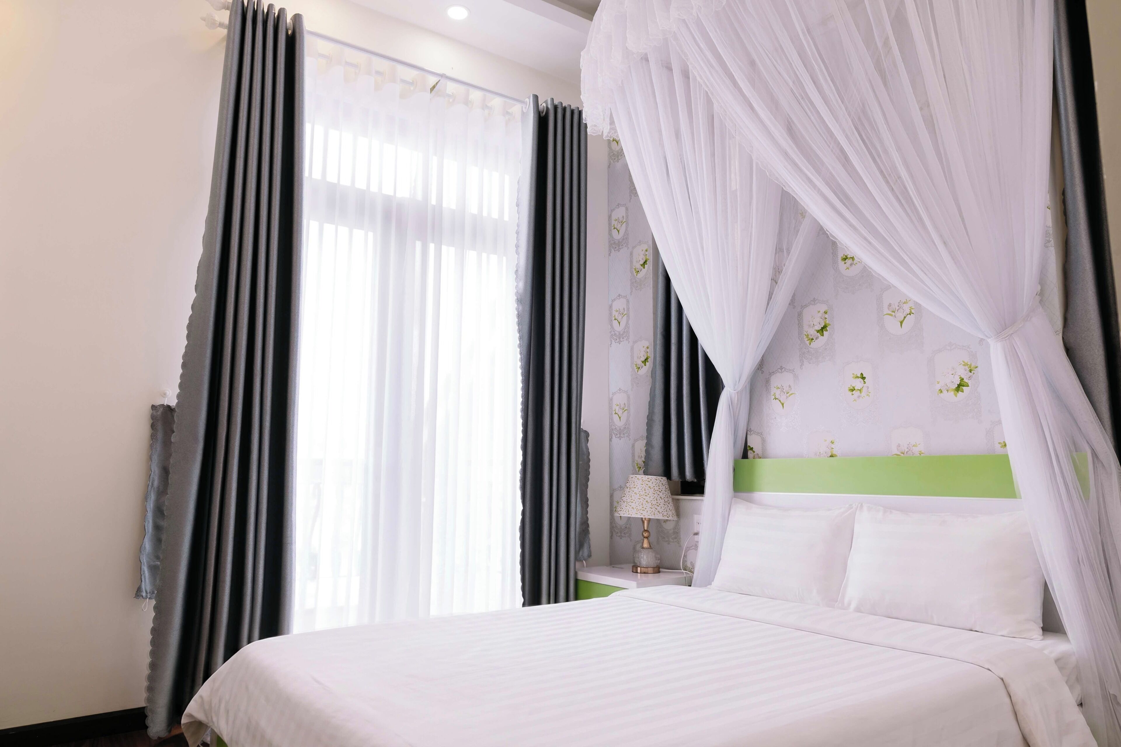 Une chambre d’hôtel avec un lit, une table de chevet, une lampe et une fenêtre avec des rideaux.