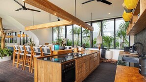 A modern kitchen with a central island, wooden bar seating, and large windows. - Brand-New LUX 5BR Villa with Grand Pool & Garden (Kerobokan)