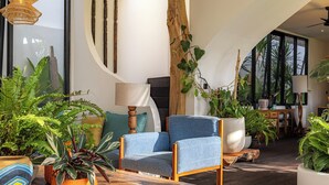 A modern living room with a blue armchair, wooden coffee table, and various potted plants. - Brand-New LUX 5BR Villa with Grand Pool & Garden (Kerobokan)