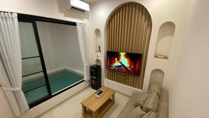 Una sala de estar con un amplio ventanal corredera, un televisor de pantalla plana montado en un panel de madera, una mesa de centro de madera y un sofá color beige.