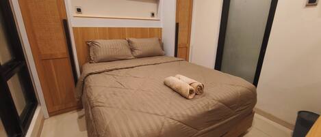 A neatly made bed with a brown bedspread and pillows, a wooden headboard, and a small wooden shelf above the bed.