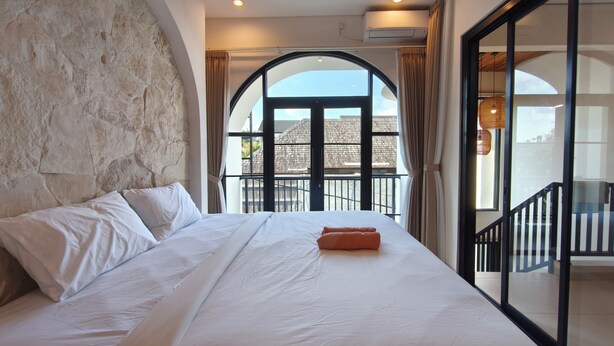 Un dormitorio con una cama grande, una pared de piedra, un balcón con vistas y un equipo de aire acondicionado.