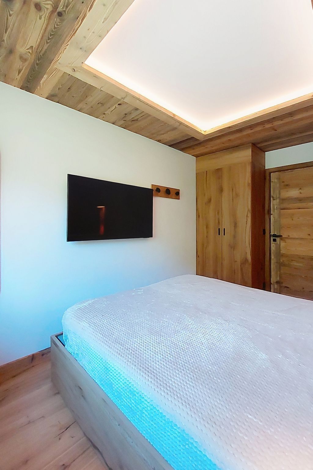 A bedroom with a bed, a mounted TV, wooden walls, and a ceiling light.