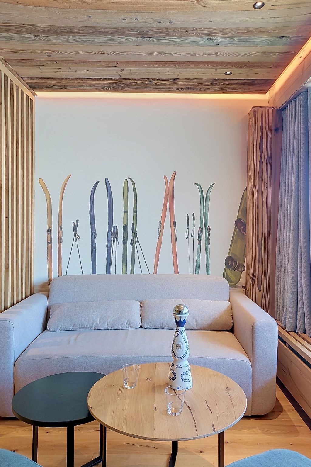 Ein Wohnzimmer mit einer Couch, einem runden Holztisch und einer Wand mit Skiern.