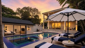 Ein Poolbereich mit Liegestühlen, ein kleines Gebäude mit Glastür und ein überdachter Sitzbereich.