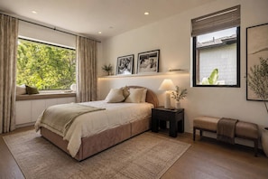 A bedroom with a bed, bedside table, bench, window, and artwork. - Sierra Bonita (Los Angeles)