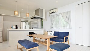 Une cuisine moderne dotée d’un îlot central, de luminaires suspendus et d’un coin repas avec des chaises et des bancs recouverts d’un tissu bleu.