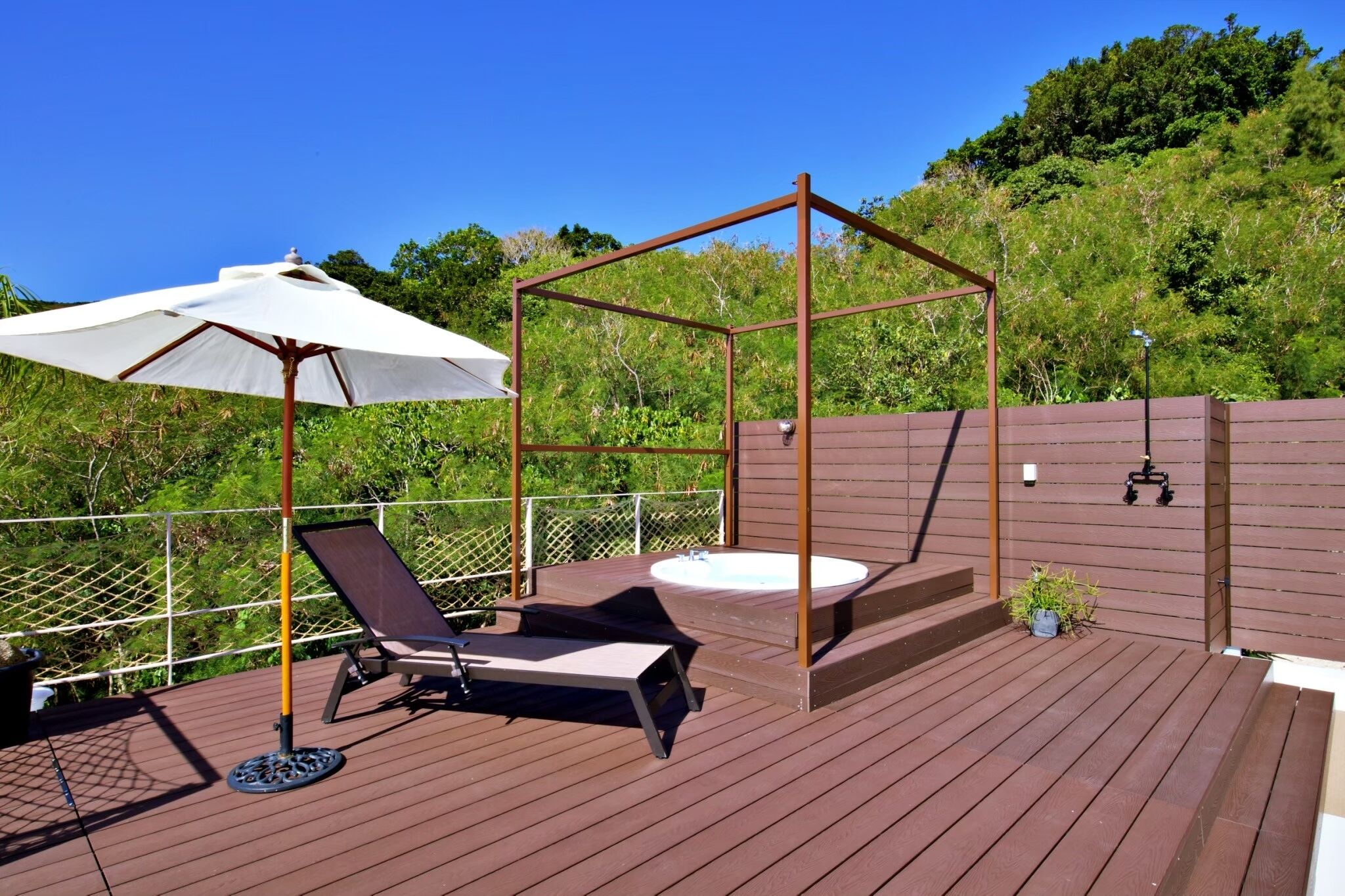 Una terraza de madera con un jacuzzi, una silla colgante y una sombrilla.