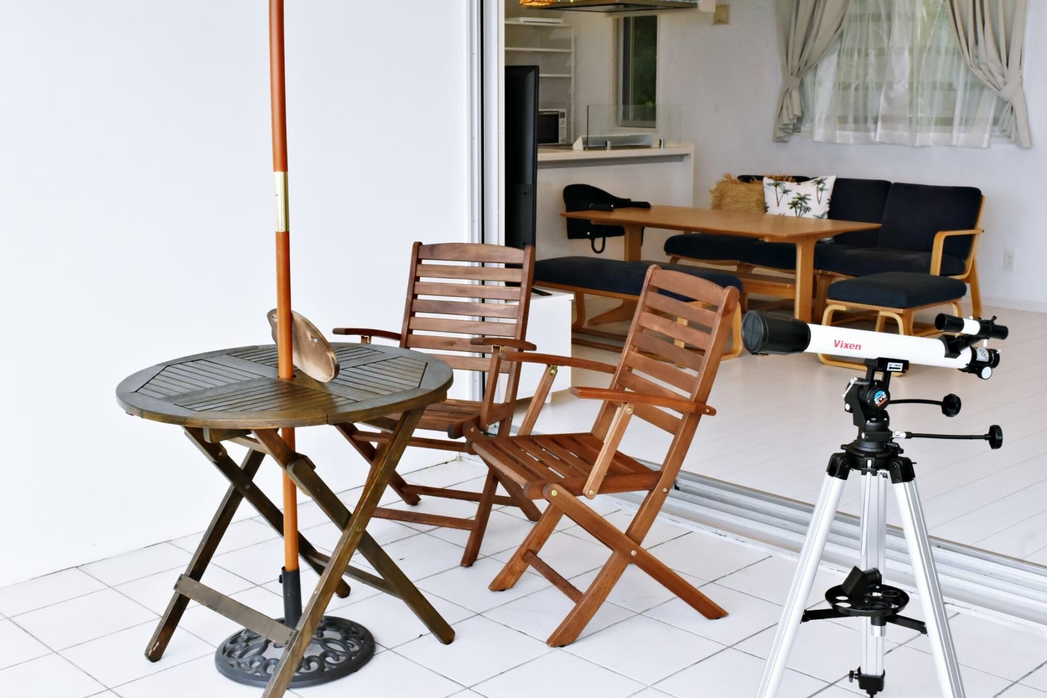 A dining area with a round table and four wooden chairs, a tripod-mounted telescope, and a sofa in the background.
