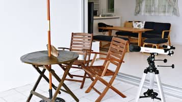 A dining area with a round table and four wooden chairs, a tripod-mounted telescope, and a sofa in the background.