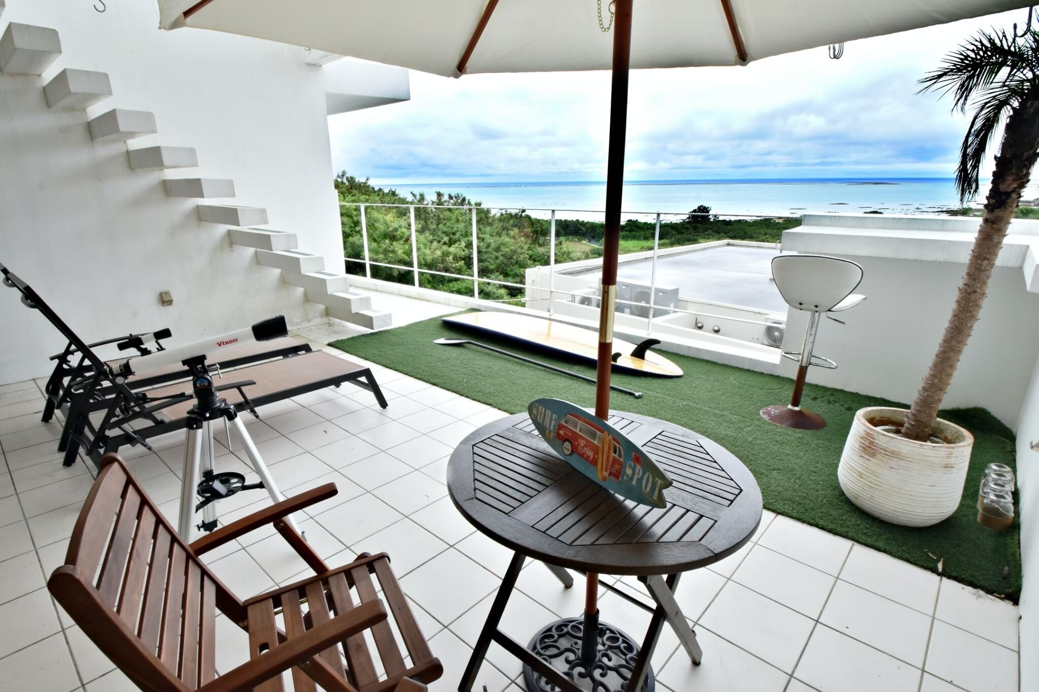 A terrace with a table and chairs, a telescope, and a view of the ocean.