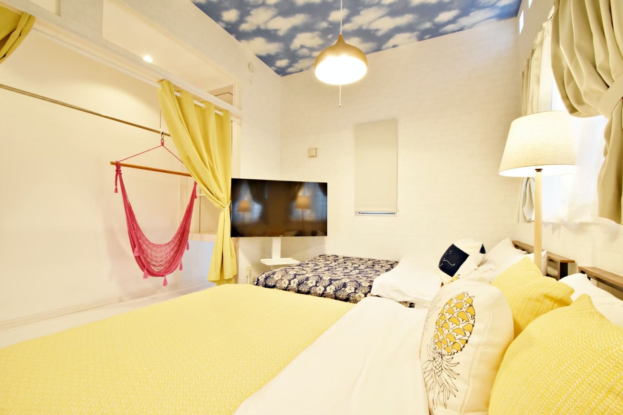 Een hotelkamer met een bed, een televisie, een hangstoel en een plafond met een wolkenmotief.