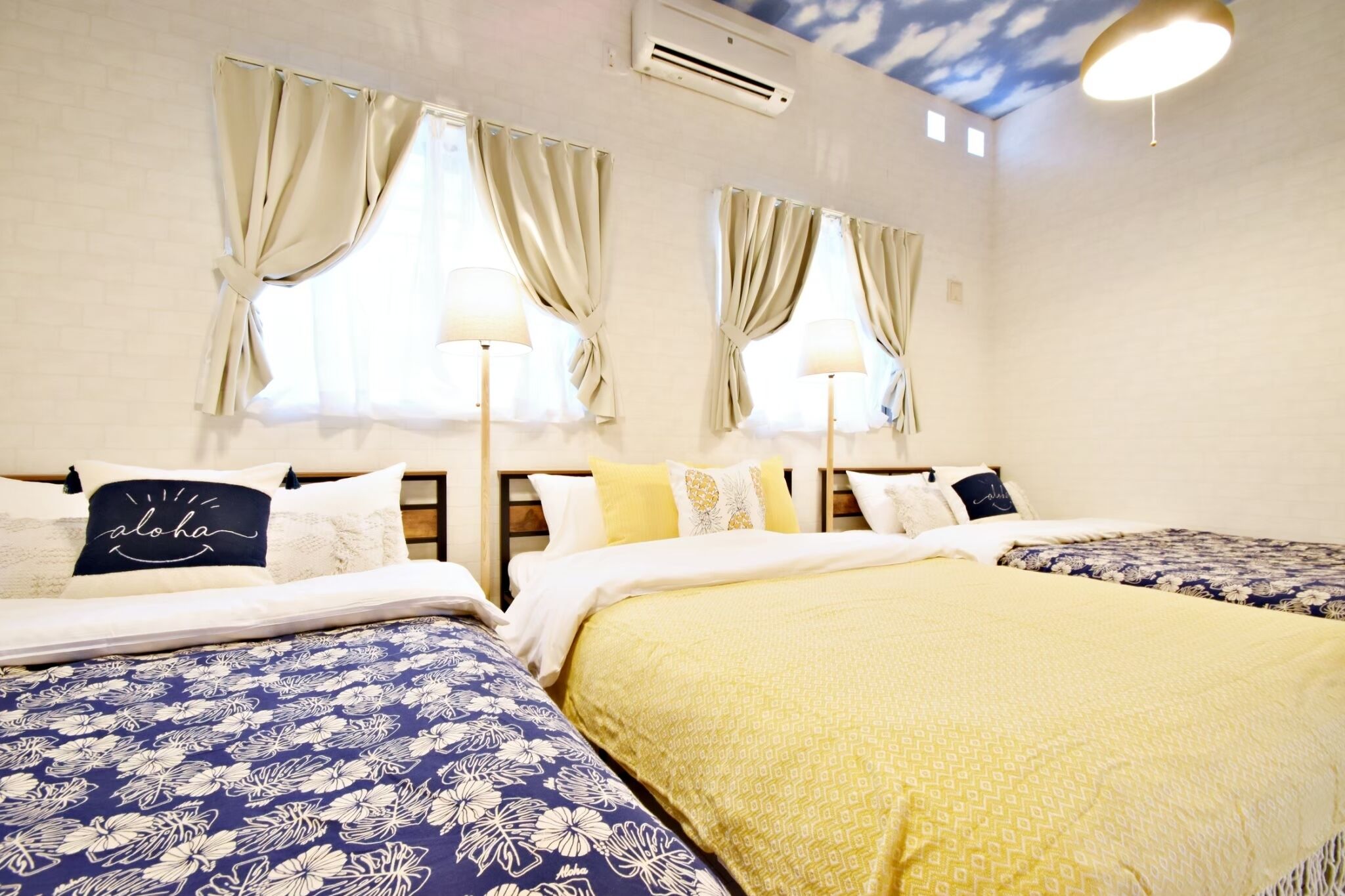 A hotel room with two beds, each with a different patterned bedspread, a ceiling with a cloud design, and a wall-mounted air conditioner.