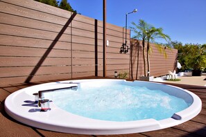 Un jacuzzi con cubierta de madera, una valla y una palmera al fondo.