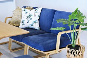 Un sofá azul con un cojín tejido, una mesa de madera y una planta en maceta.