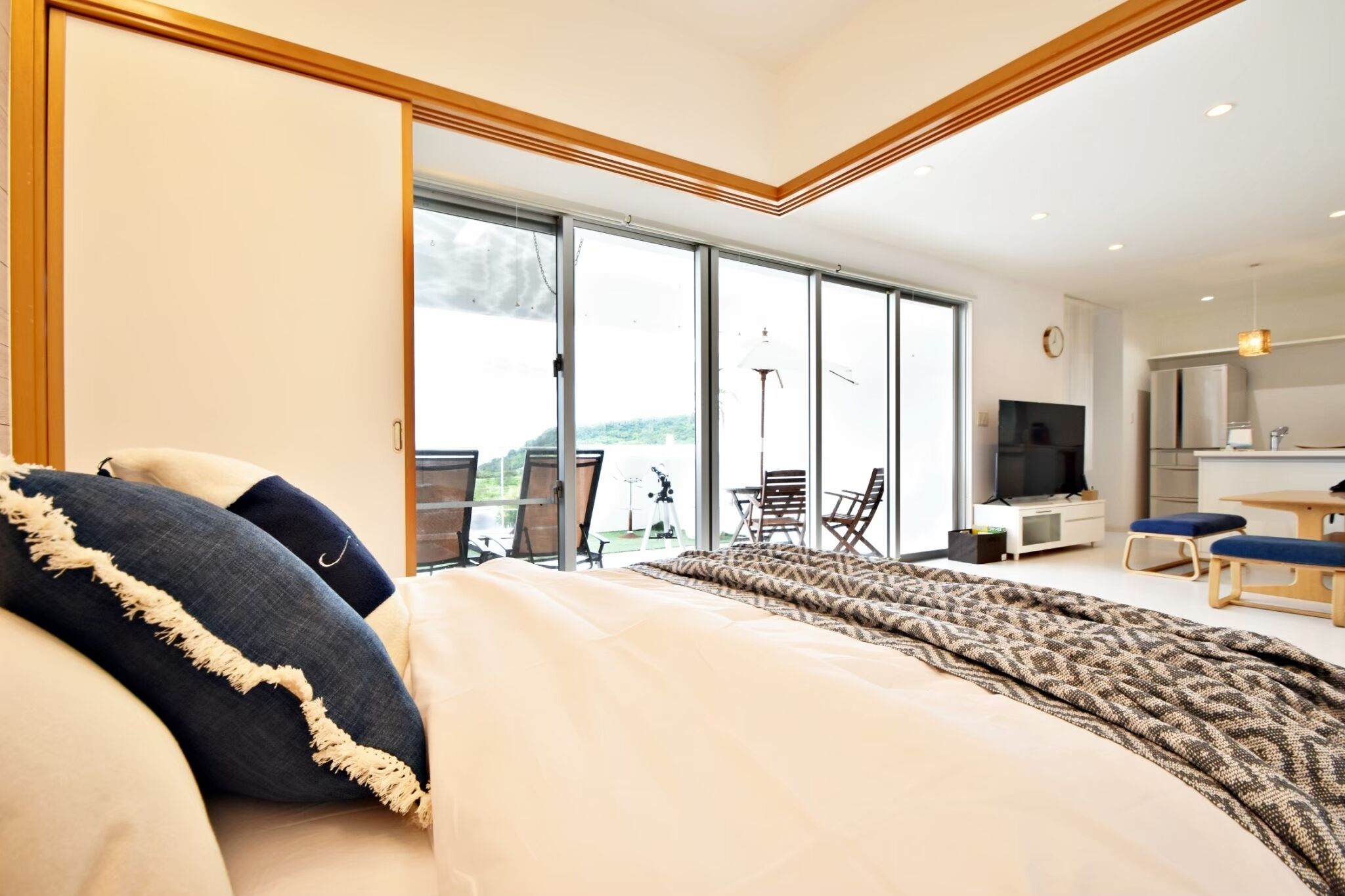 A modern bedroom with a large bed, a view of the outdoors, a dining area, and a kitchen.