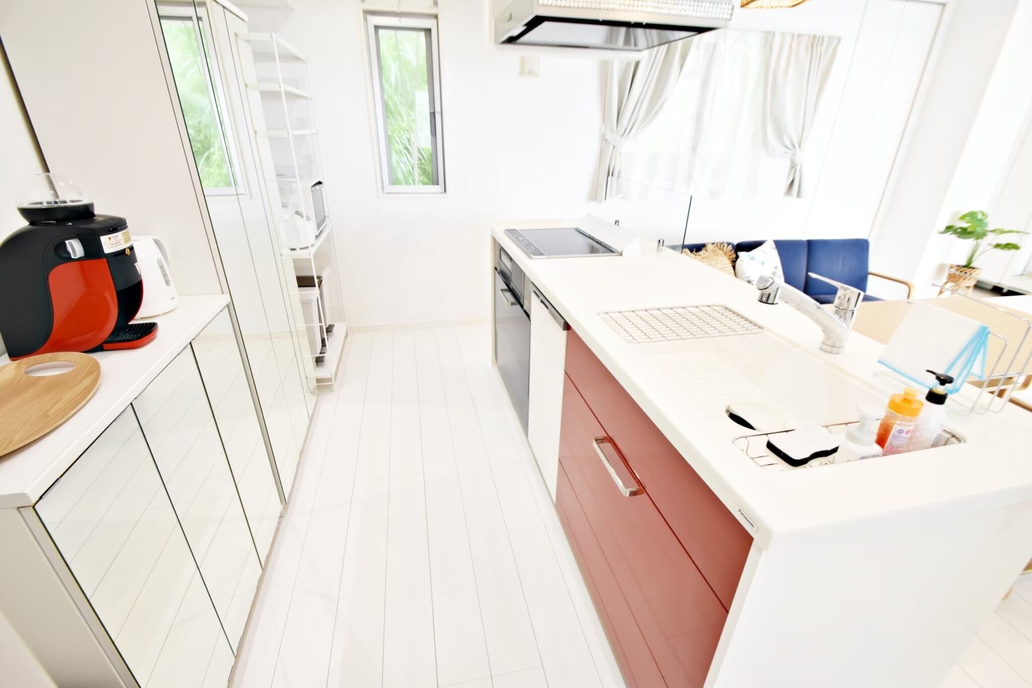 Une cuisine moderne avec des meubles blancs, un plan de travail rouge, un four encastré et une fenêtre donnant sur un paysage verdoyant.