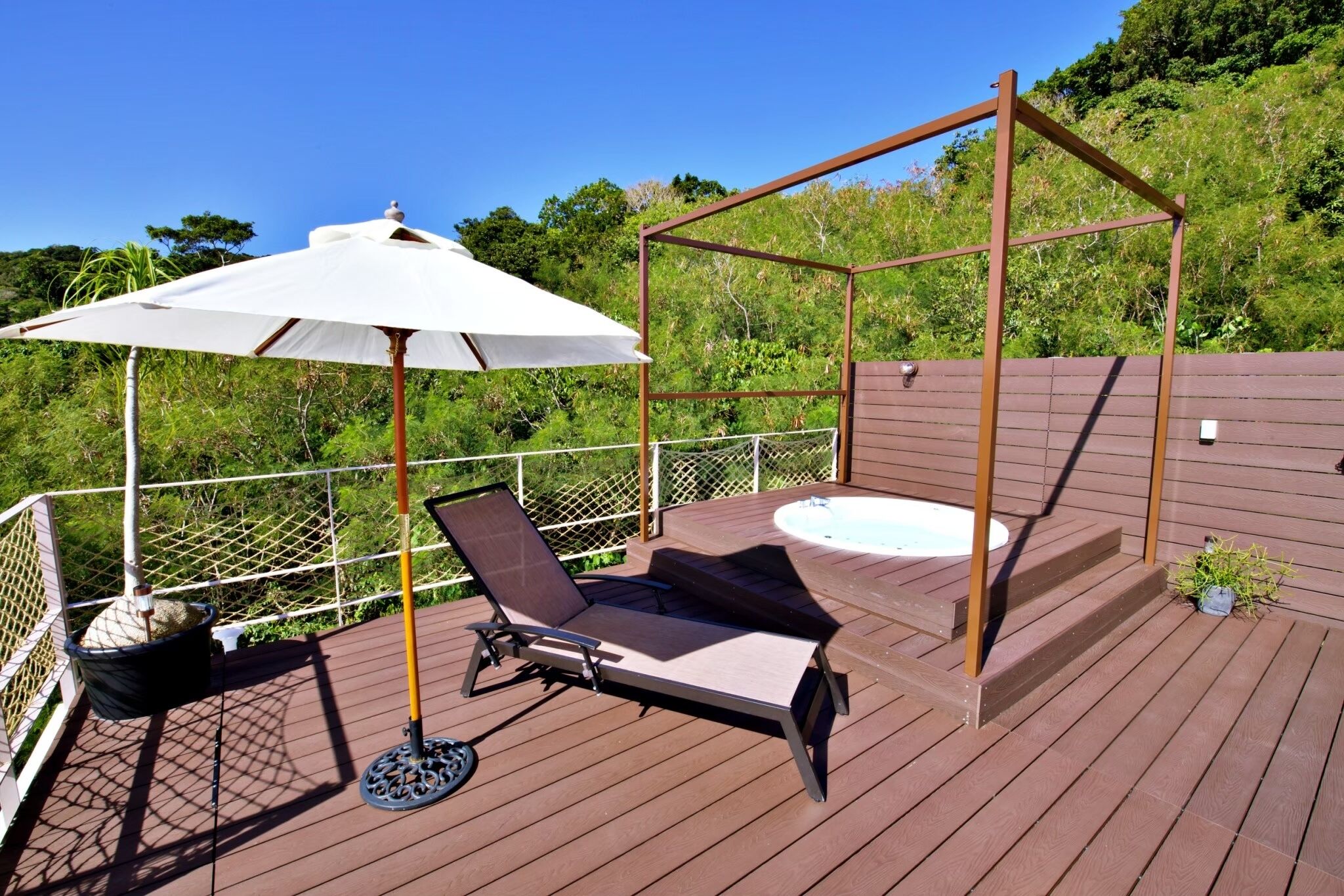 A wooden deck with a hot tub, a lounge chair, and a canopy umbrella.