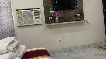 A hotel room with a bed, a wall-mounted TV, an air conditioning unit, and a power outlet.