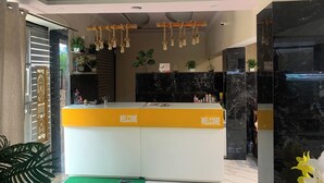 Un comptoir d’accueil avec des panneaux indiquant « BIENVENUE », un tapis vert et une plante.