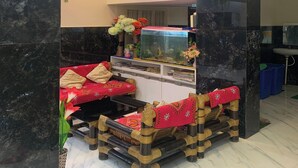 Une pièce avec un sol en marbre noir, un canapé rouge orné de coussins à motifs, un aquarium et un lavabo.