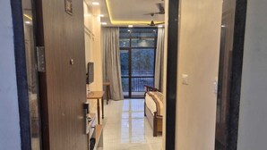 Un couloir d’hôtel avec une porte en bois, un banc, une petite table et une vue à travers une grande fenêtre.