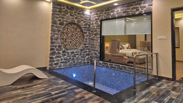 Une salle de bain moderne avec un mur en pierre, une mosaïque circulaire, une piscine aux carreaux bleus et un espace de douche clos par des parois de verre.