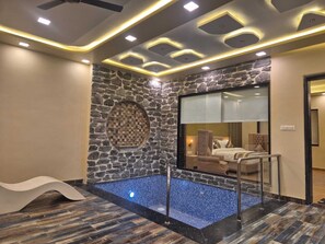 A modern bathroom with a stone wall, a circular mosaic, a blue tiled pool, and a glass-enclosed shower area. - Shivay Resort (Pushkar)