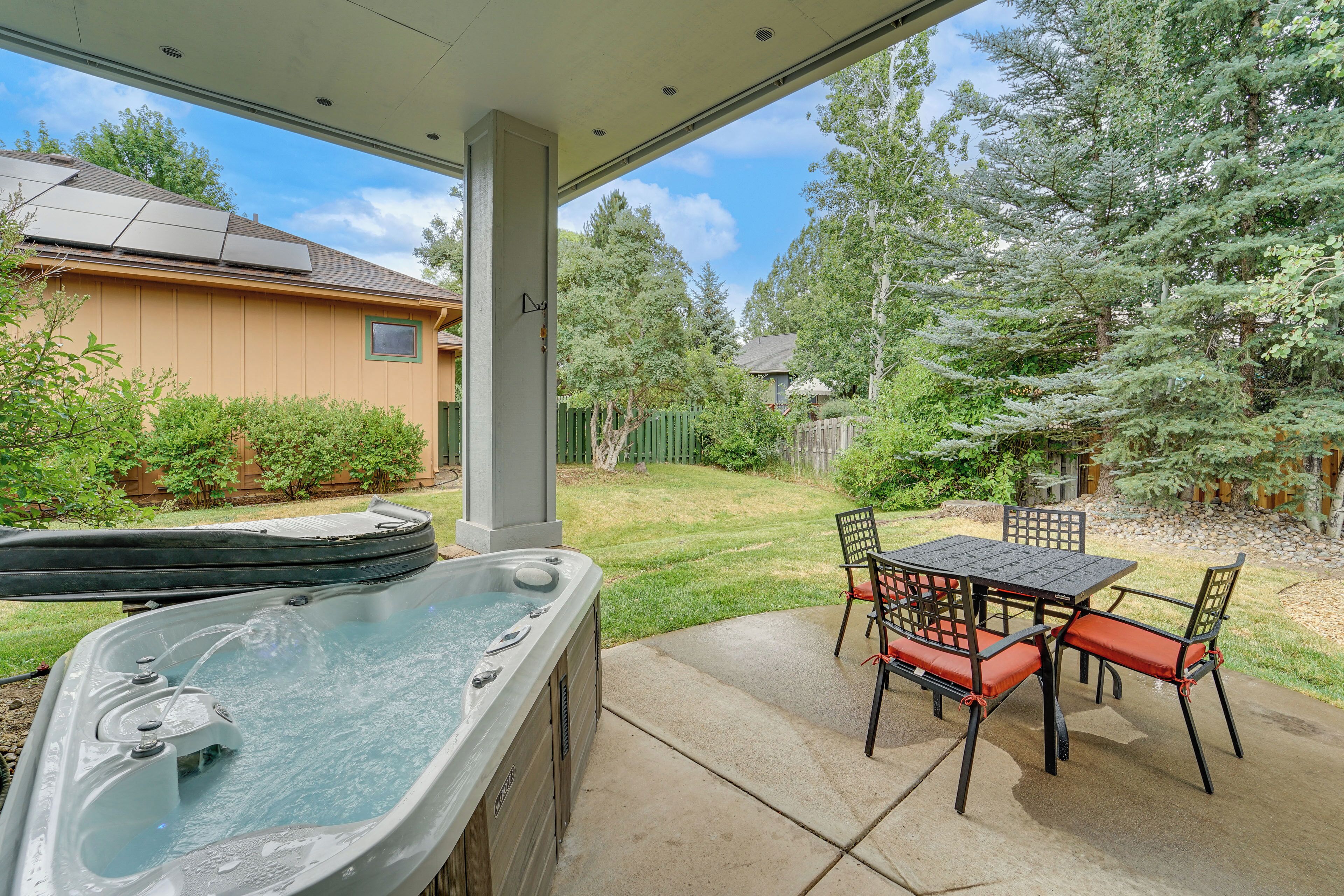 Un bain à remous avec une table et des chaises, un patio couvert et une vue sur un jardin avec des arbres et une clôture.