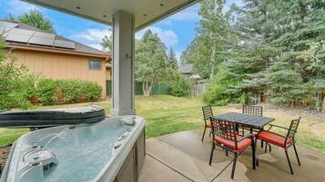 Un bain à remous avec une table et des chaises, un patio couvert et une vue sur un jardin avec des arbres et une clôture.