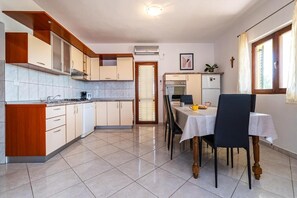 Una cuina funcional amb armaris de fusta, una taula de dinar amb caires i un refrigerador petit.