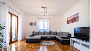 Una sala de estar moderna con un sofá modular, un televisor de pantalla plana y un piso de madera con patrón de espiga.