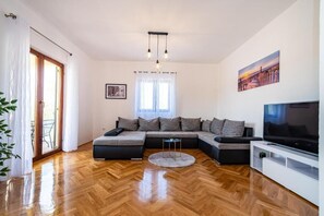 Ein modernes Wohnzimmer mit einem Ecksofa, einem Flachbildfernseher und einem Fischgrätenparkettboden.