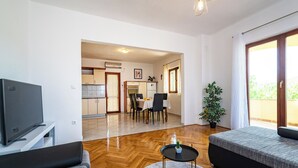 Una sala de estar moderna con un televisor de pantalla plana, un sofá, una mesa redonda de centro y una zona de comedor con una mesa y sillas.